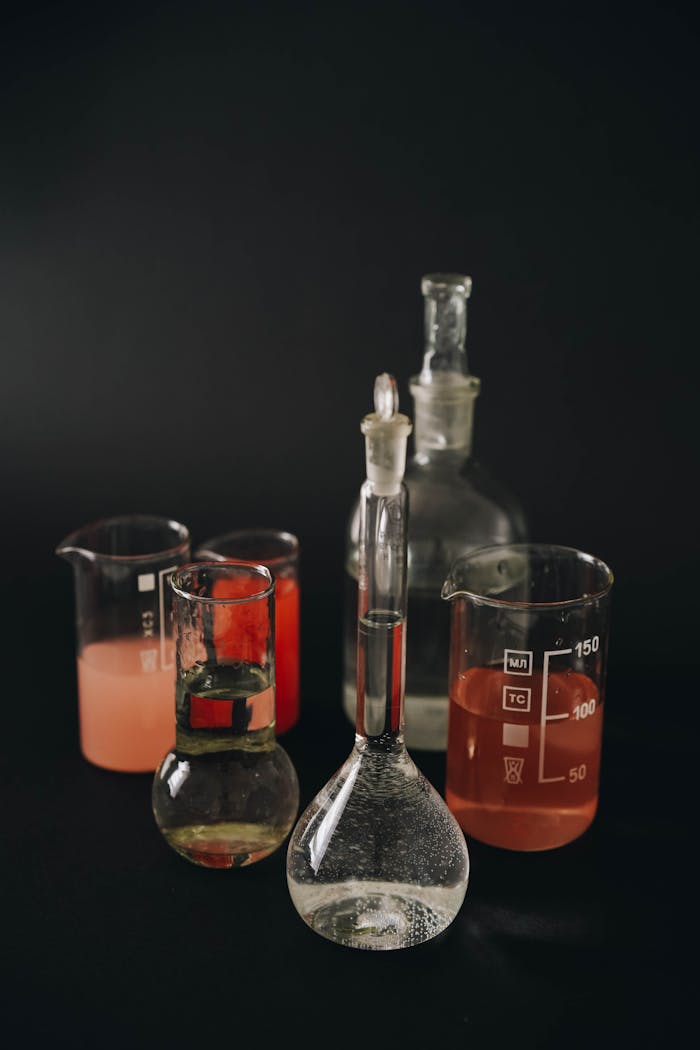 A collection of laboratory glassware with colored liquids on a dark background.